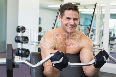 Shirtless smiling bodybuilder lifting heavy barbell weight using