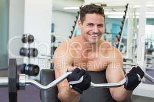 Shirtless smiling bodybuilder lifting heavy barbell weight using