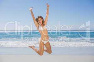 Fit smiling woman in white bikini leaping on beach