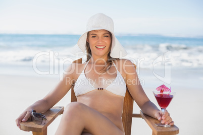 Pretty blonde relaxing in deck chair on the beach with cocktail