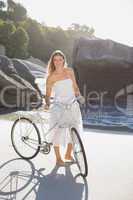 Beautiful blonde in white sundress standing with bike on the bea