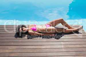 Fit woman in pink bikini lying poolside