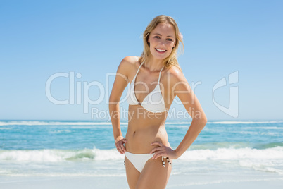 Beautiful blonde in white bikini smiling at camera on the beach