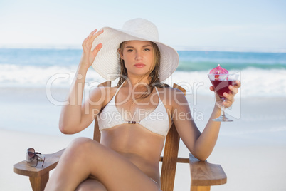 Pretty blonde relaxing in deck chair on the beach with cocktail