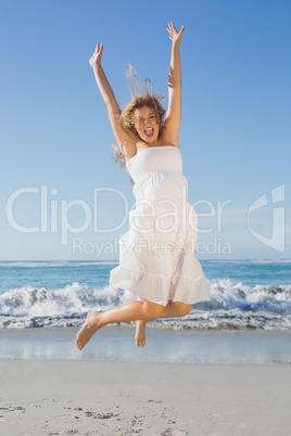 Beautiful blonde in white sundress jumping up on the beach