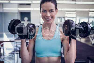 Smiling woman lifting heavy dumbbells