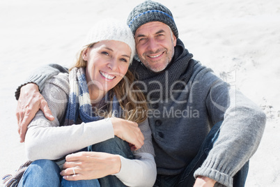 Attractive couple smiling at camera on the beach in warm clothin