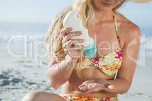 Pretty blonde woman sitting on the beach applying suncream