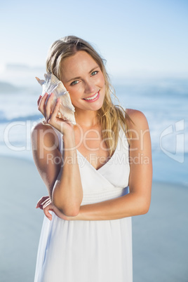 Pretty blonde standing at the beach in white sundress listening