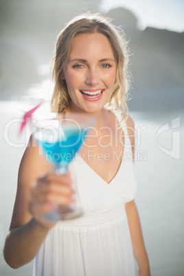 Smiling blonde standing at the beach in white sundress with blue