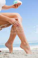 Woman rubbing sunblock on her leg at the beach