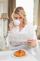 Pretty blonde in bathrobe drinking coffee and reading newspaper