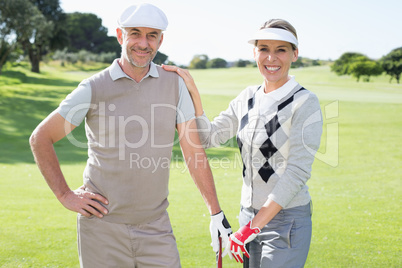 Golfing couple smiling at camera and holding clubs