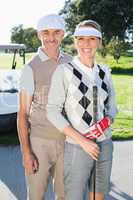 Happy golfing couple looking at camera with golf buggy behind