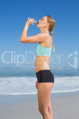 Fit woman standing on the beach drinking water