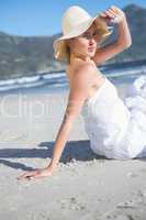 Content blonde in white dress sitting on the beach looking to ca