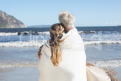 Couple wrapped up in blanket on the beach looking out to sea