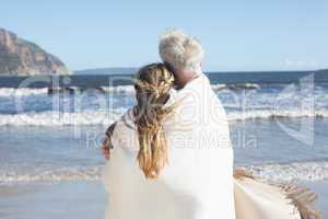 Couple wrapped up in blanket on the beach looking out to sea