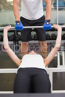 Fit woman lifting barbell with her trainer spotting