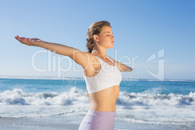 Sporty blonde standing on the beach with arms out