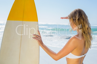 Blonde surfer in white bikini holding her board on the beach
