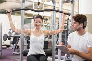 Fit brunette using weights machine for arms with trainer taking