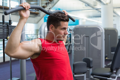 Handsome bodybuilder using weight machine for arms