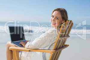 Gorgeous blonde sitting on deck chair using laptop on beach