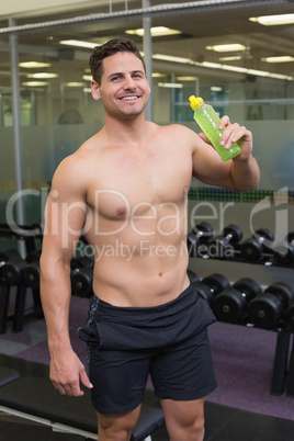 Shirtless bodybuilder drinking sports drink smiling at camera