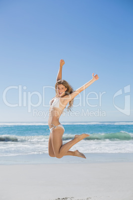 Fit smiling woman in white bikini leaping on beach