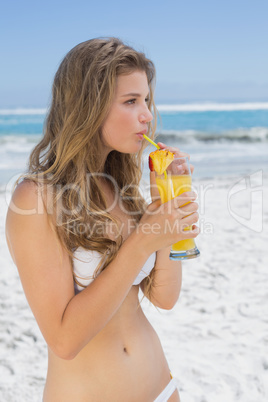 Pretty blonde in white bikini sipping cocktail on the beach