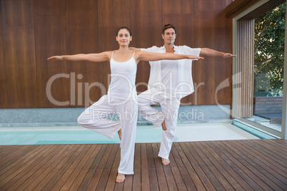 Peaceful couple in white doing yoga together in tree position