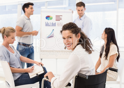 Casual businesswoman in wheelchair smiling at camera during meet