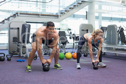 Bodybuilding man and woman lifting kettlebells in a squat