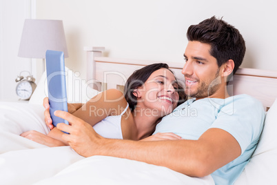 Attractive couple lying in bed with tablet pc