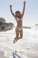 Beautiful smiling woman in white bikini leaping on the beach