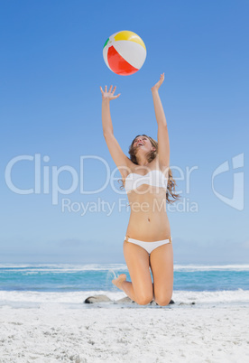 Fit blonde in white bikini throwing beach ball