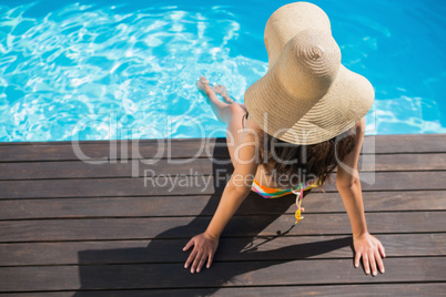 Beautiful brunette in bikini sitting by the pool paddling