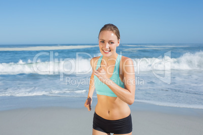 Fit woman smiling and jogging on the beach