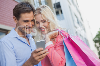 Stylish young couple looking at smartphone holding shopping bags