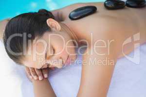 Relaxed brunette lying poolside having a hot stone massage