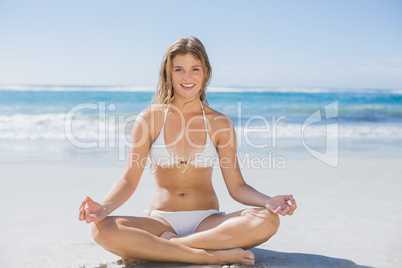 Beautiful girl in white bikini sitting in lotus pose on beach