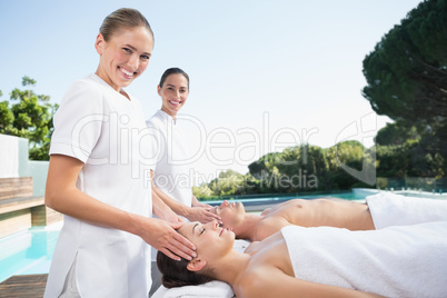 Masseuses smiling at camera while massaging couple