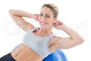 Fit woman doing sit ups on blue exercise ball smiling at camera
