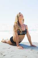 Fit blonde in cobra pose on the beach