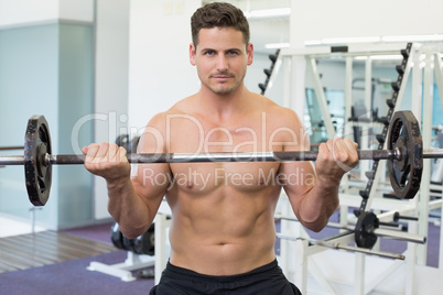 Shirtless bodybuilder lifting heavy barbell weight looking at ca