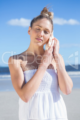 Pretty blonde in white dress listening to conch on the beach