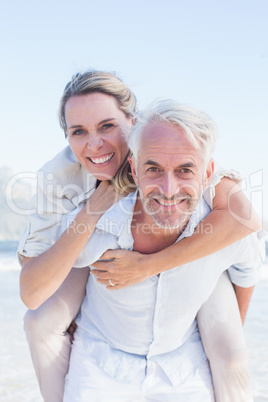 Man giving his smiling wife a piggy back at the beach