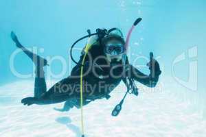 Woman on scuba training submerged in swimming pool showing thumb