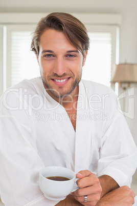 Handsome man having breakfast in his bathrobe drinking coffee